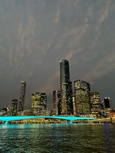 the city skyline is lit up at night with bright blue lights and clouds in the sky