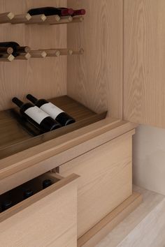 two bottles of wine sitting on top of a wooden shelf next to a drawer with drawers