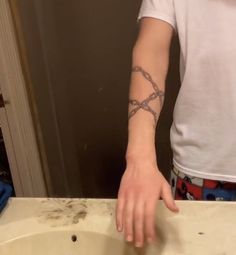 a person with a cross tattoo on their arm standing in front of a bathroom sink