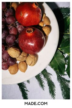 an apple, walnuts and grapes on a white plate with pine cones next to it