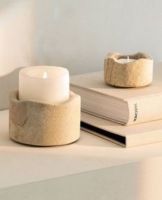 two books and a lit candle on a white table with light coming from the top