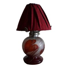 a lamp with a red shade on it sitting on top of a table next to a white wall