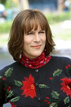 a woman wearing a black sweater with red poinsettis on it and a red scarf around her neck