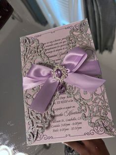 a person holding up a purple and silver wedding card with a bow on it's side