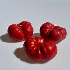 three red tomatoes sitting next to each other on a white counter top with a lit candle in the middle