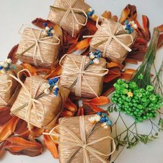 small wrapped gift boxes with blue flowers and greenery next to them on a white surface