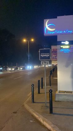 an empty street at night with cars driving on the road and signs in front of it