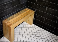 a wooden bench sitting on top of a white tile floor next to a black tiled wall