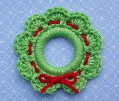 a green crocheted brooch with red ribbon around it on a blue background