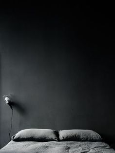 a black and white photo of a bed in a dark room with a lamp on the side