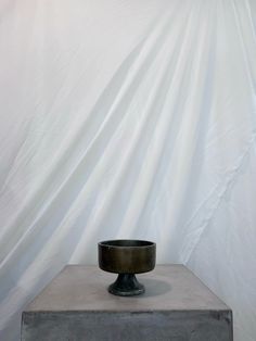 a black bowl sitting on top of a cement block in front of a white backdrop