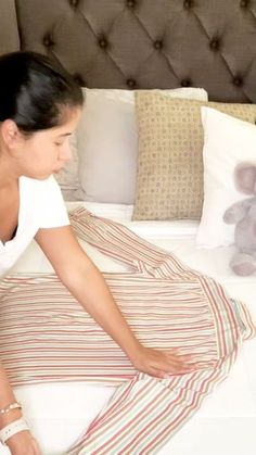 a woman sitting on top of a bed next to a stuffed animal and pillows in front of her