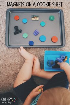 a toddler playing with buttons on the floor next to a play tray filled with magnets