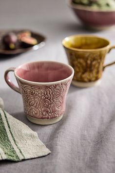 three cups sitting on top of a table next to plates with food in the background