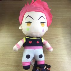 a stuffed doll with pink hair and yellow eyes sitting on a wooden table next to a card