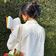 a woman reading a book in front of a hedge