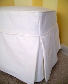 a white bed skirt sitting on top of a carpeted floor next to a yellow wall