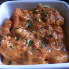 a white bowl filled with pasta covered in sauce and garnished with parsley