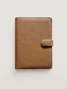 a brown leather notebook with a clip on the front and one side, sitting on a white surface