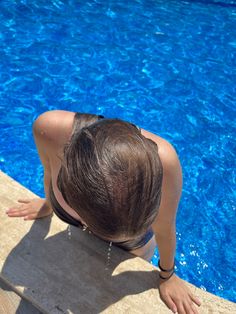 a woman sitting on the edge of a swimming pool with her hands in the water