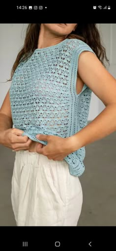 a woman wearing a blue crochet top is holding her hands on her hip