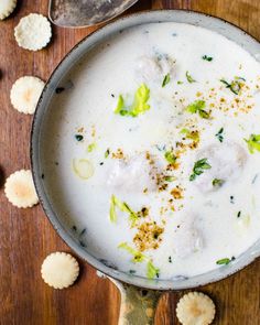 a bowl filled with soup next to crackers on top of a wooden table and two spoons