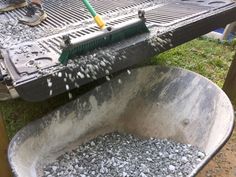 a bucket filled with gravel next to a metal grate on top of a grass covered field