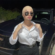 a woman wearing sunglasses standing in front of a car with her hands on her hips