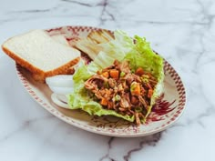 a plate topped with lettuce and meat next to a slice of bread on top of a table