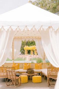 an outdoor seating area with white drapes and yellow stools