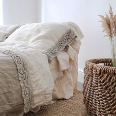 a bed with white linens and ruffled bedspread next to a wicker basket