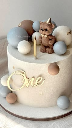 a birthday cake with a teddy bear and one candle on the top that says one