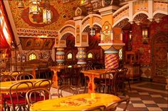 an ornately decorated restaurant with yellow and red tables, chairs and lamps hanging from the ceiling