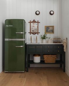 a green refrigerator sitting next to a sink in a room with white walls and wooden floors