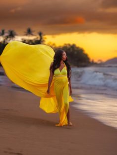 a woman in a yellow dress is walking on the beach with her long flowing fabric