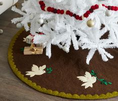 a white christmas tree decorated with red and gold ornaments on a brown rug in a living room