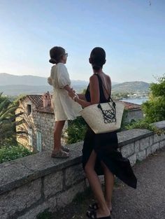 two women standing next to each other on top of a stone wall with a basket