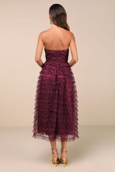 the back of a woman wearing a purple dress with ruffled layers and high heels