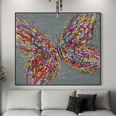 a living room with a white couch and painting on the wall above it that has multicolored butterflies