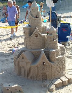 a sand castle made to look like it is on the beach with people standing around