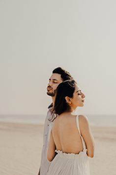 a man and woman standing on top of a sandy beach next to the ocean in white dresses