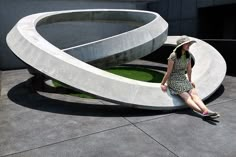 a woman sitting on the ground in front of a sculpture with grass growing out of it