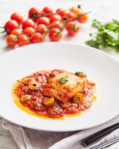 a white plate topped with meat covered in marinara sauce and garnished with tomatoes