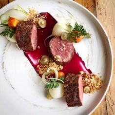 a white plate topped with meat and veggies on top of a wooden table