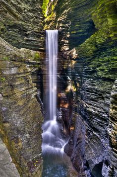 a small waterfall in the middle of a narrow canyon with green moss growing on it's sides