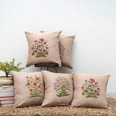 four pillows with embroidered flowers on them sitting next to a book and potted plant