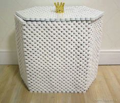 a white wicker basket with a gold crown on top sitting on a wooden floor