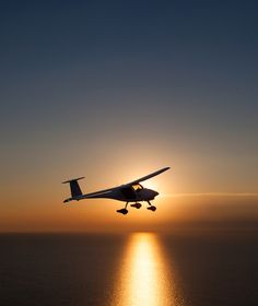 an airplane is flying low over the ocean at sunset with the sun in the background