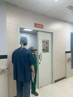 two doctors in scrubs standing at the door to an operating room that is empty