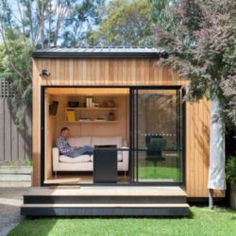 a man sitting on top of a white couch in a small garden shed with sliding glass doors